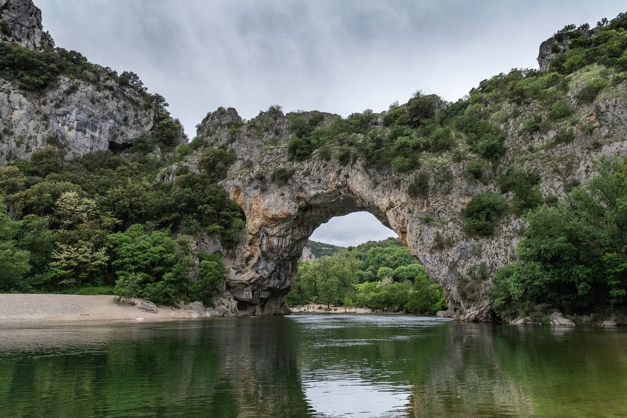 A propos Scenic view of the natural arch at Vallon-Pont-dArc, France, over a tranquil river.